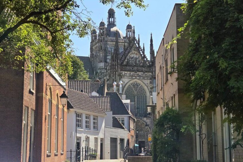 A historic church with Gothic architecture, a narrow street lined with buildings, and a clear blue sky. 1