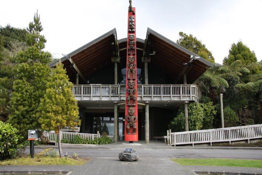 A building with a wooden facade and a balcony, surrounded by trees and a red pole with carvings. 2
