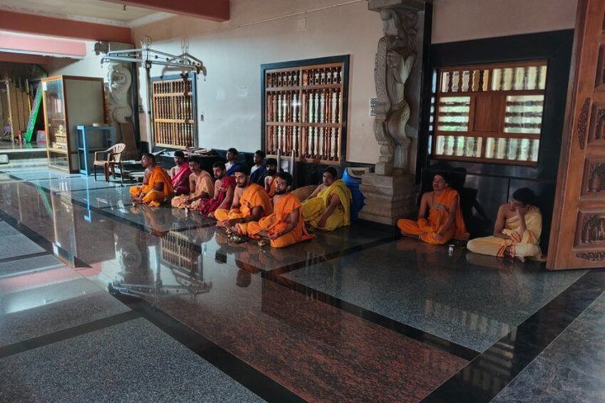 Monks sitting in a temple with stone carvings and a polished floor. 3