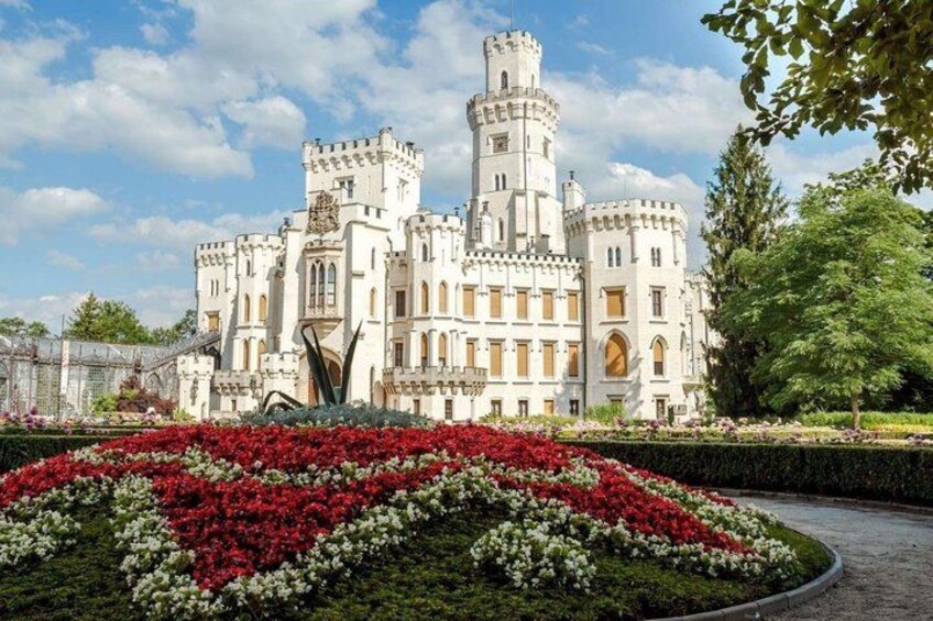 A castle with a tower, surrounded by a garden with red and white flowers. 1