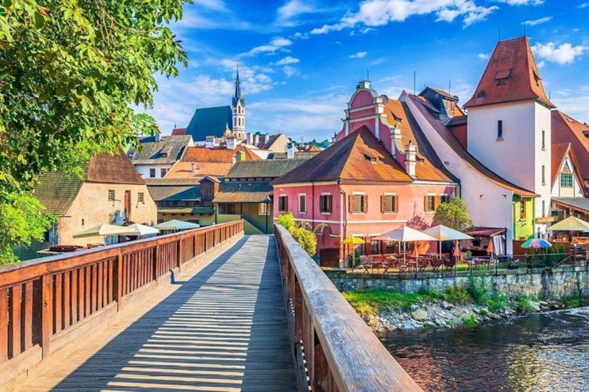 A wooden bridge over a river, colorful buildings, and a church spire in the background. 5