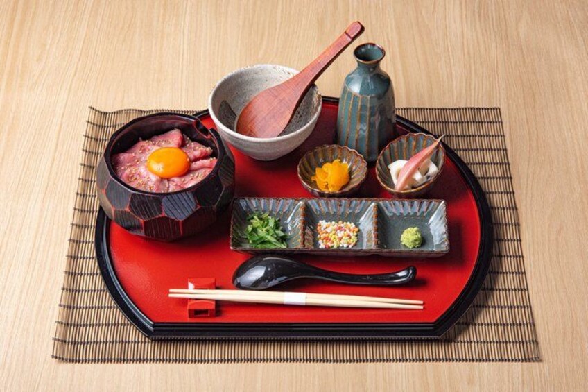A traditional Japanese meal setup with a red tray, chopsticks, a bowl of raw meat, a wooden spoon, and small dishes of condiments and vegetables. 4