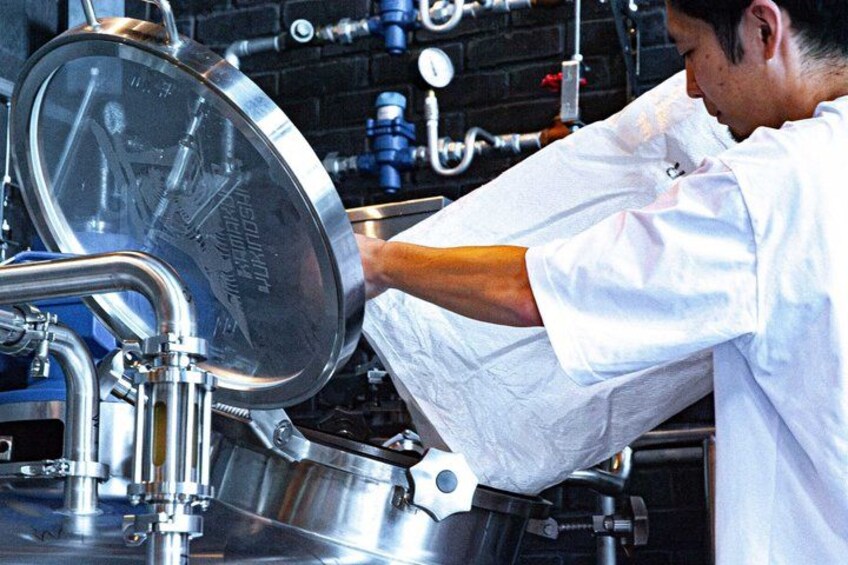 A person in a white shirt working with stainless steel equipment, possibly in a kitchen or industrial setting. 5