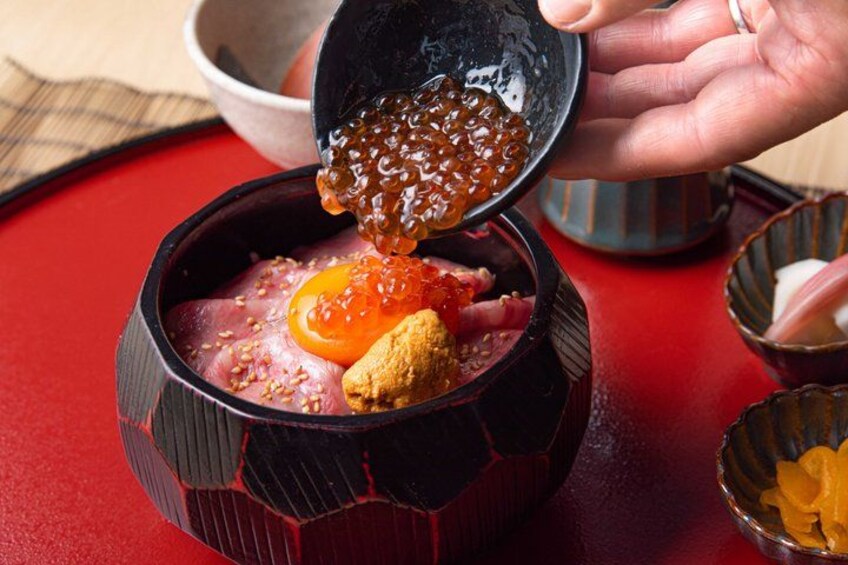 A person pouring caviar onto a dish with meat and a cherry. 3