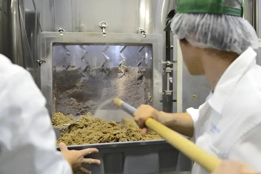 A person in a white uniform and hairnet stirring a mixture in a large industrial container. 3