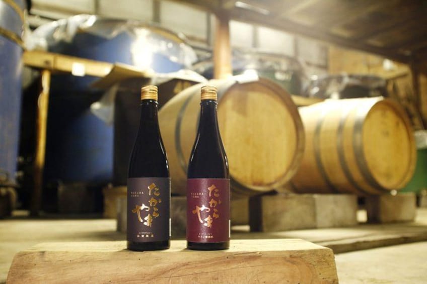 Two bottles of wine on a wooden surface with barrels in the background. 1