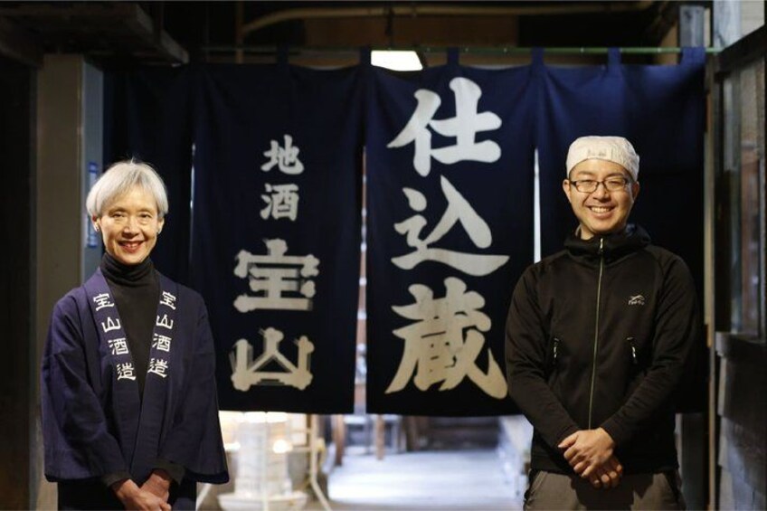 Two individuals standing in front of a banner with Japanese characters. 3
