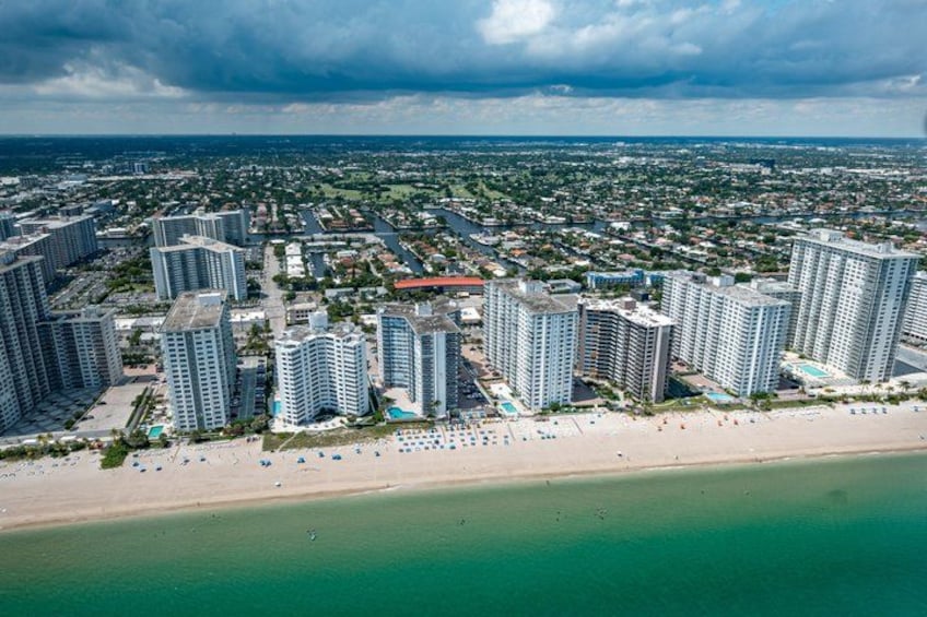 A coastal cityscape with high-rise buildings, a beach, and a clear sky. 5