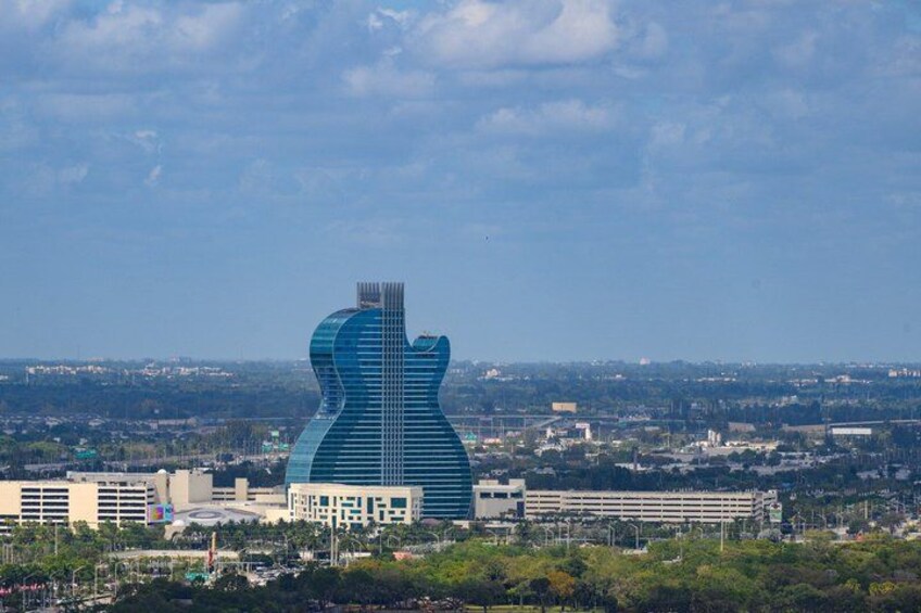 A large building shaped like a guitar, surrounded by a cityscape with various other buildings and greenery. 3