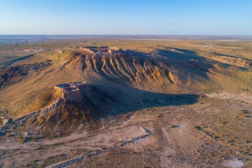 A vast desert landscape with a prominent hill and a small settlement at its base. 1