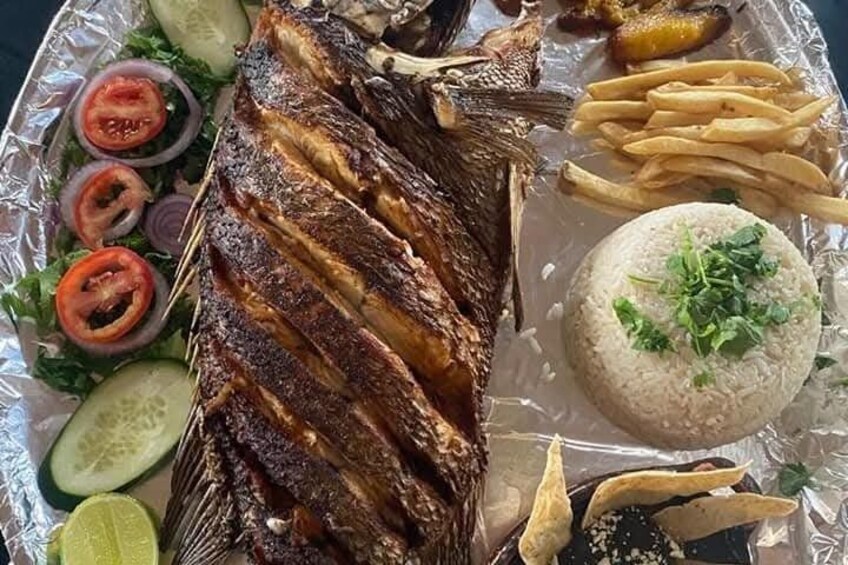 A whole grilled fish with skin on, served with French fries, rice, and a side salad. 3