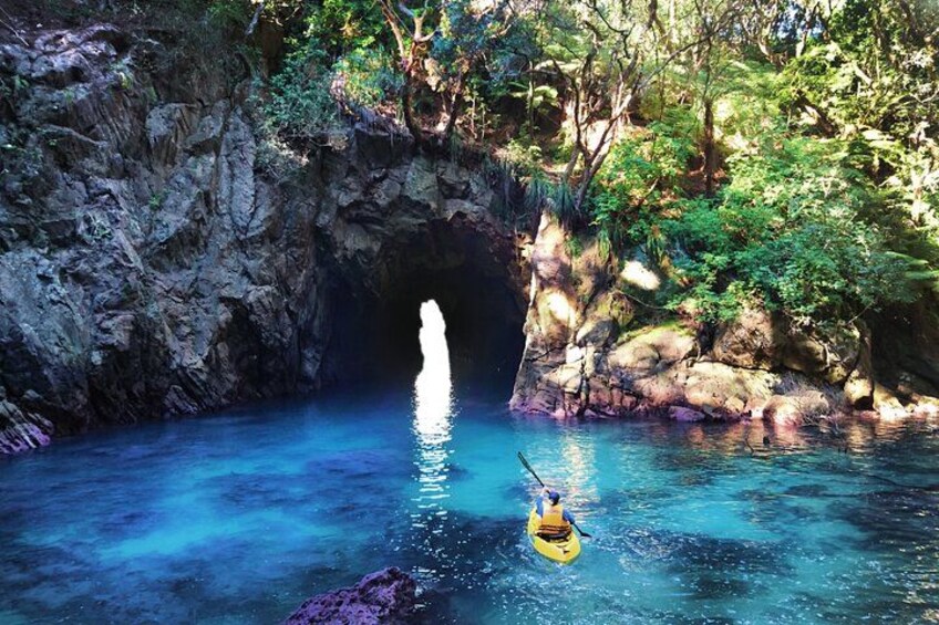 A kayaker in a clear blue river, a rocky cliff, and lush greenery. 1