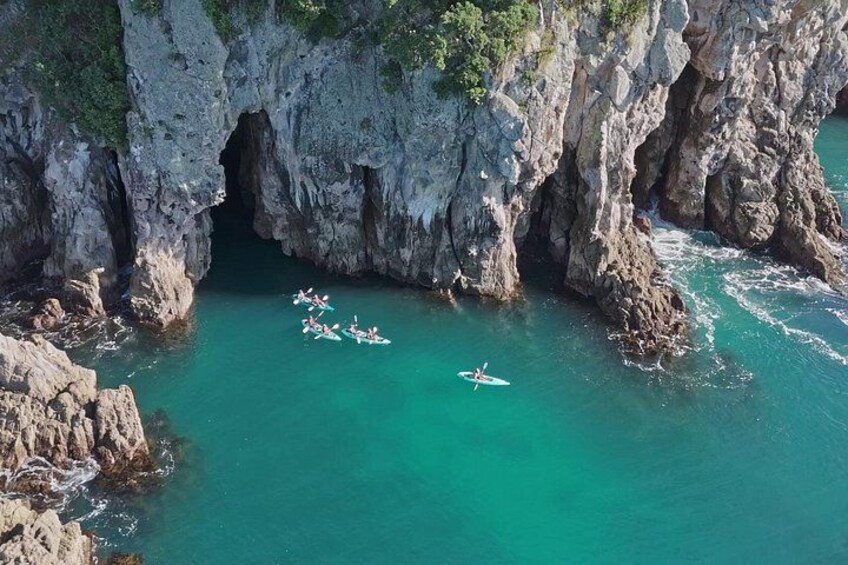 A group of kayaks in a turquoise sea with rocky cliffs. 3