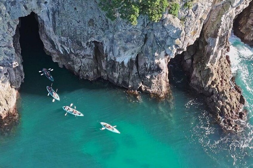 A group of kayaks in a turquoise sea near a rocky cliff. 4