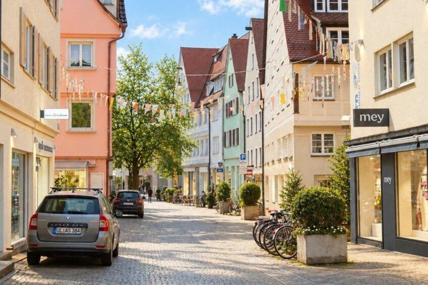 A cobblestone street lined with colorful buildings, a parked car, and a bicycle. 3