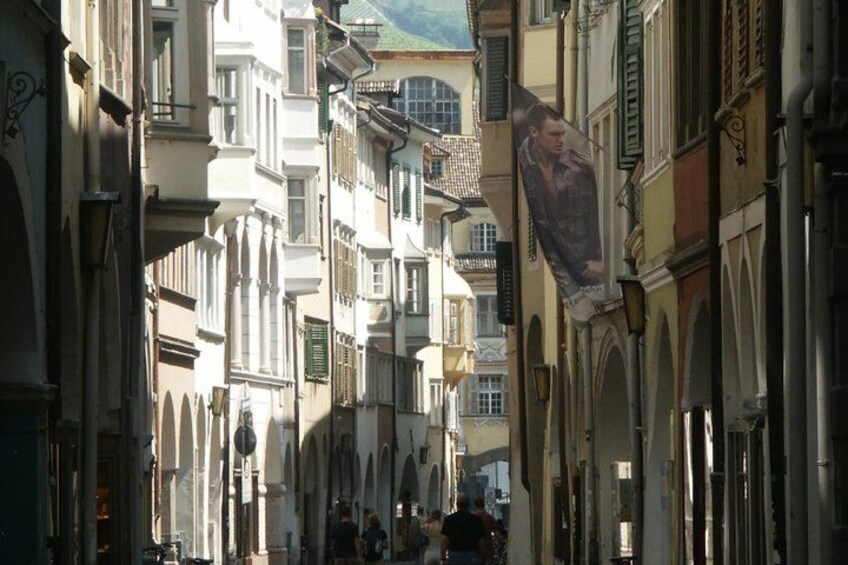 A narrow street lined with historic buildings, a prominent banner, and a green hill in the background. 5