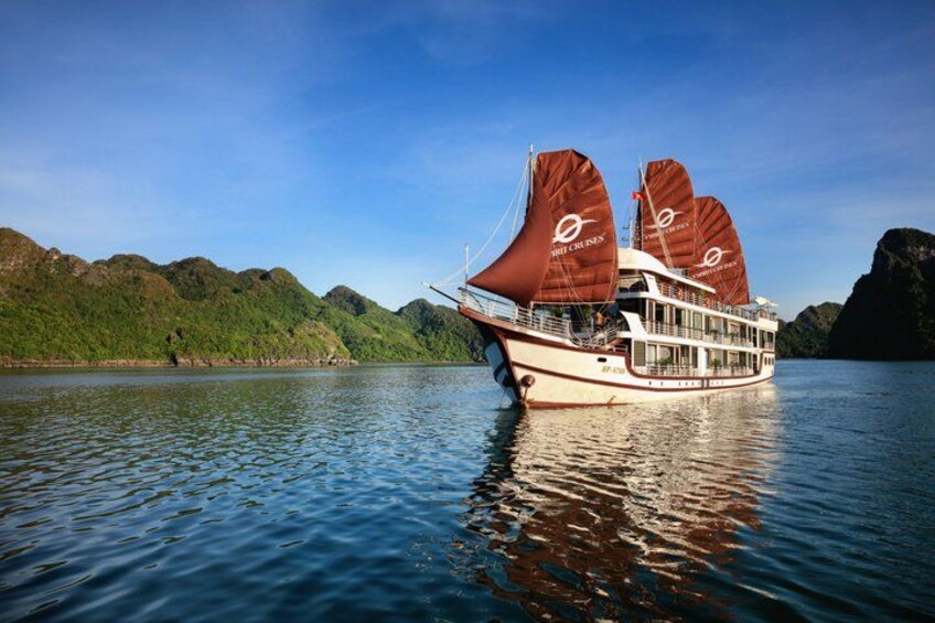 A traditional sailing boat with two large sails on a calm lake surrounded by green hills. 1