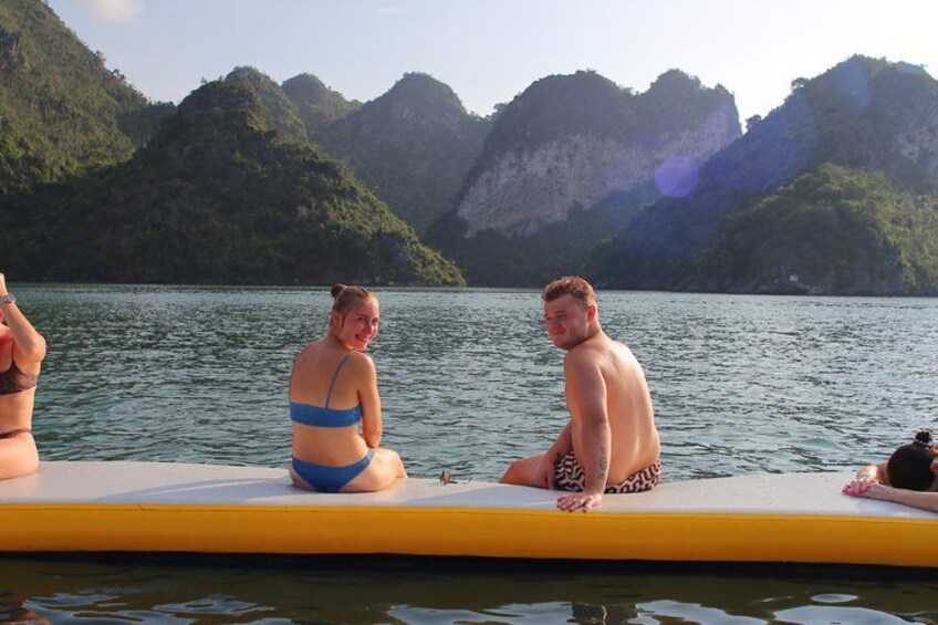 Two people sitting on a yellow floating platform in a body of water with mountains in the background. 3