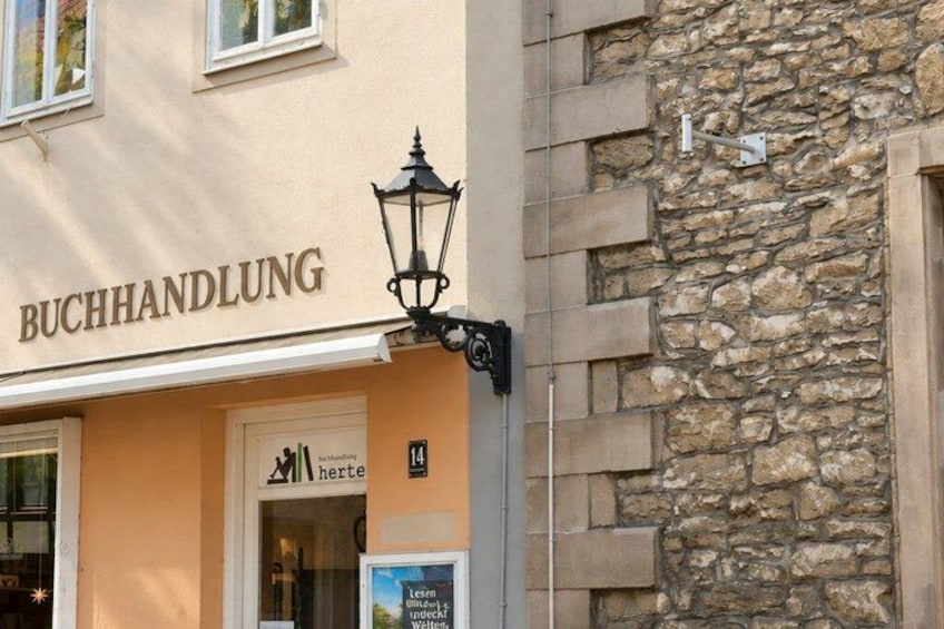 A building with a sign that reads 'BUCHHANDLUNG' and a street lamp attached to the building. 4