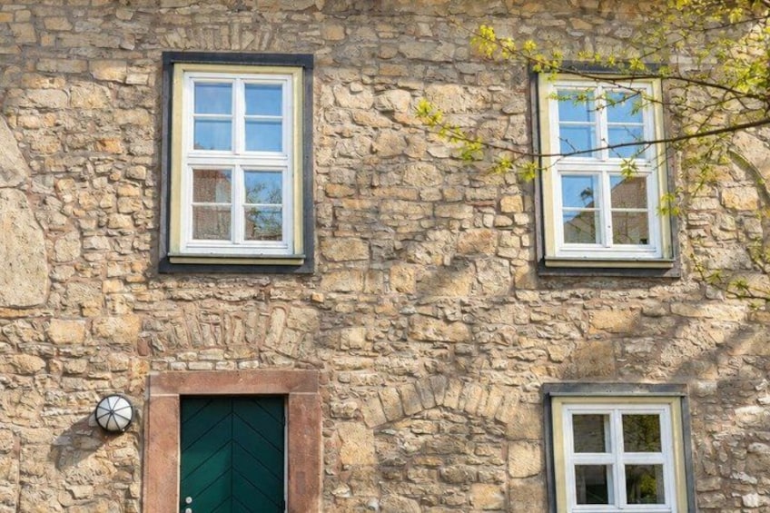 A stone building with three windows, a green door, and a clock. 3