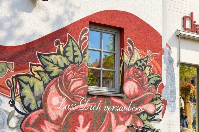 A building with a mural of red flowers and leaves, and a window. 5