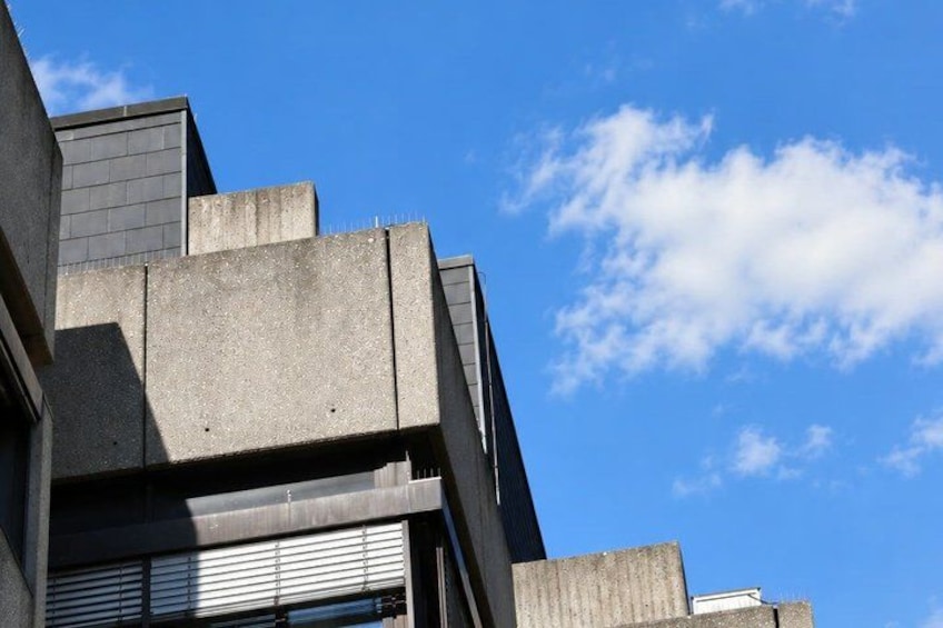 A building with a concrete facade and a sloped roof against a clear blue sky with scattered clouds. 2
