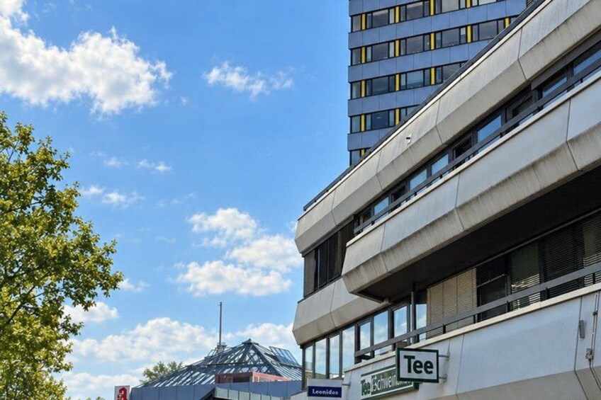 A modern building with a glass facade, a sign for 'Tee,' and a clear blue sky with clouds. 5