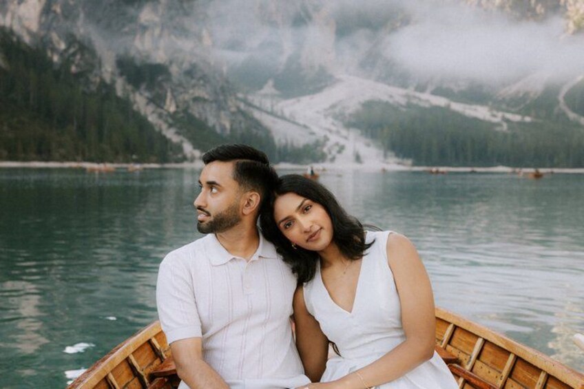 A couple in a wooden boat on a calm lake with mountains in the background. 3