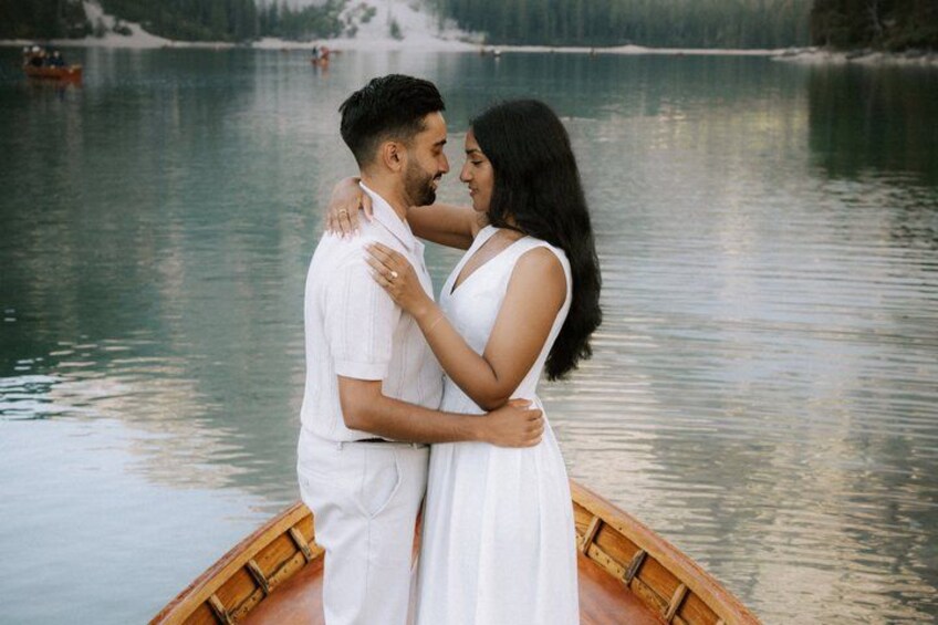 A couple embracing on a wooden boat by a calm lake with a forested shoreline in the background. 4