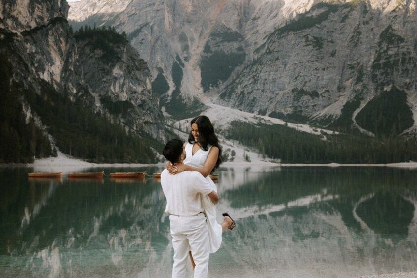 A couple embracing by a calm lake with mountains in the background. 5