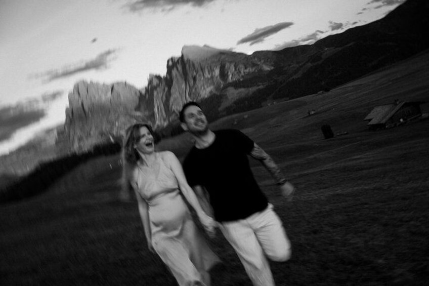 A couple walking in a mountainous area with a rocky landscape and a small building in the distance. 5