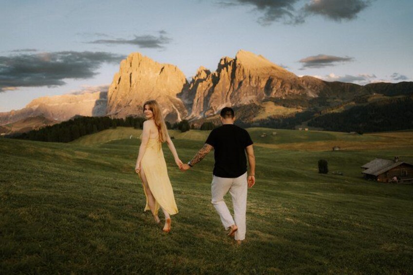 A couple walking on a grassy field with a mountain in the background. 1