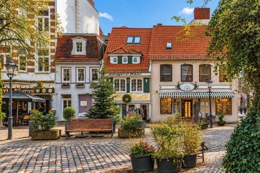 A cobblestone square with buildings, a bench, and potted plants. 2