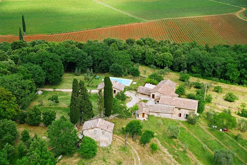 A rural landscape with terraced fields, a cluster of stone buildings, and a dense tree line. 5