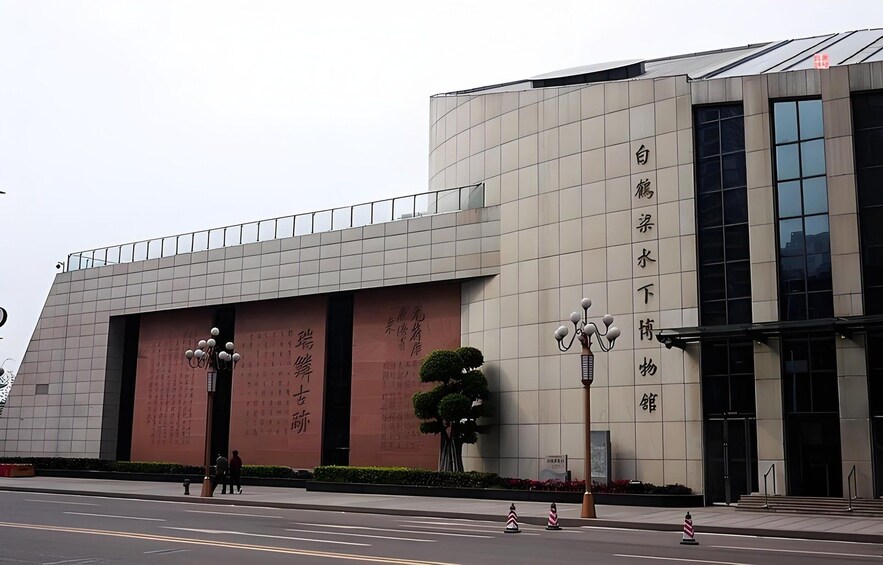 A modern building with large windows and a curved facade. There are banners with Chinese characters and a street with pedestrians. 1