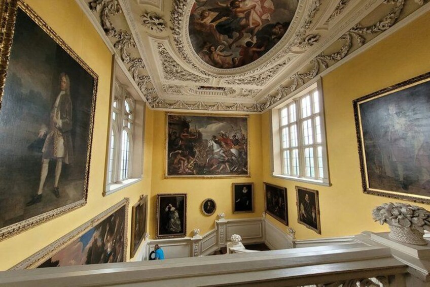 A room with classical architecture, including ornate ceiling frescoes and large framed paintings. 5