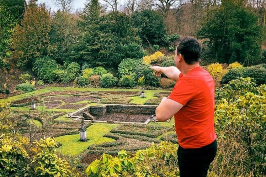 A person pointing at a terraced garden with various plants and a stone structure. 4