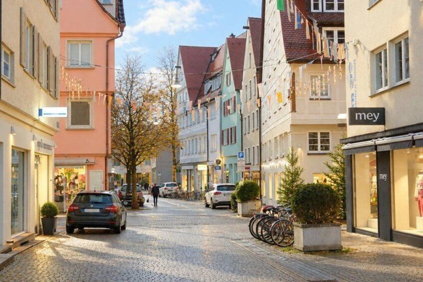 A cobblestone street lined with colorful buildings, parked cars, and bicycles. 2