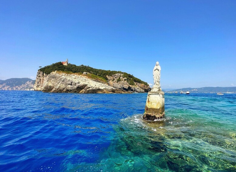 Mare blu intenso con un'isola rocciosa sullo sfondo e una statua in primo piano. 1