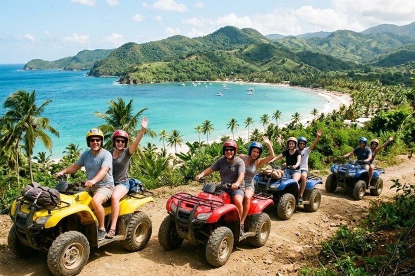 People on quad bikes on a dirt path with a beach and mountains in the background. 1