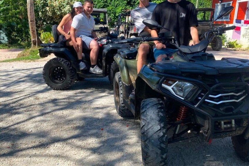 A group of people on an ATV, with a vehicle and a building in the background. 4
