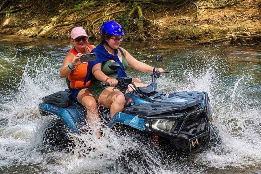 Two people on a blue ATV in a river, splashing water. 5