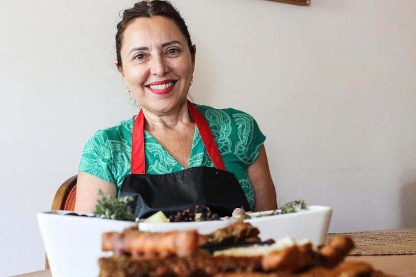 A person wearing a green patterned top and a black apron, seated at a table with a white plate containing food. 1