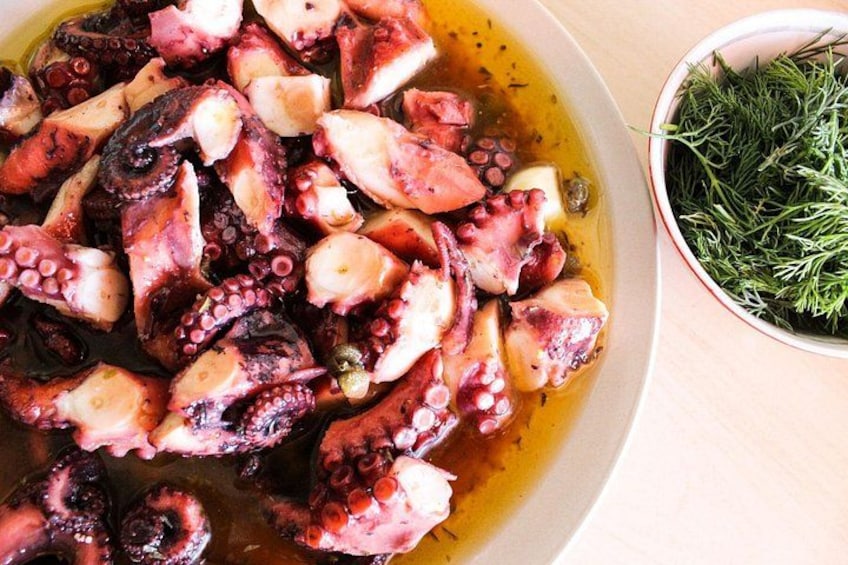 A bowl of cooked octopus with a side of fresh dill. 2