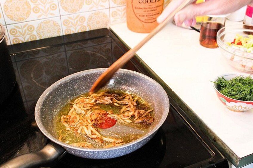 A pan on a stove with food being cooked, a bowl of chopped vegetables, and a bottle of sauce on the counter. 3