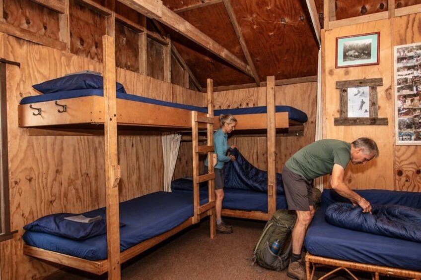 A wooden bunk bed room with a ladder, a person adjusting a mattress, and a backpack on the floor. 5