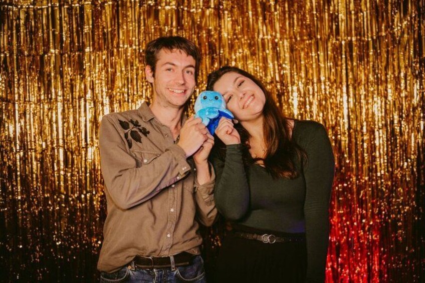 Two people holding a blue toy in front of a shiny gold backdrop. 3