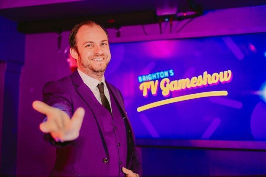 A person in a purple suit with a TV Gameshow sign in the background. 1