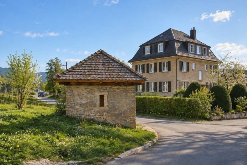A stone cottage with a tiled roof, a larger house with a pitched roof, and a curved driveway. 3