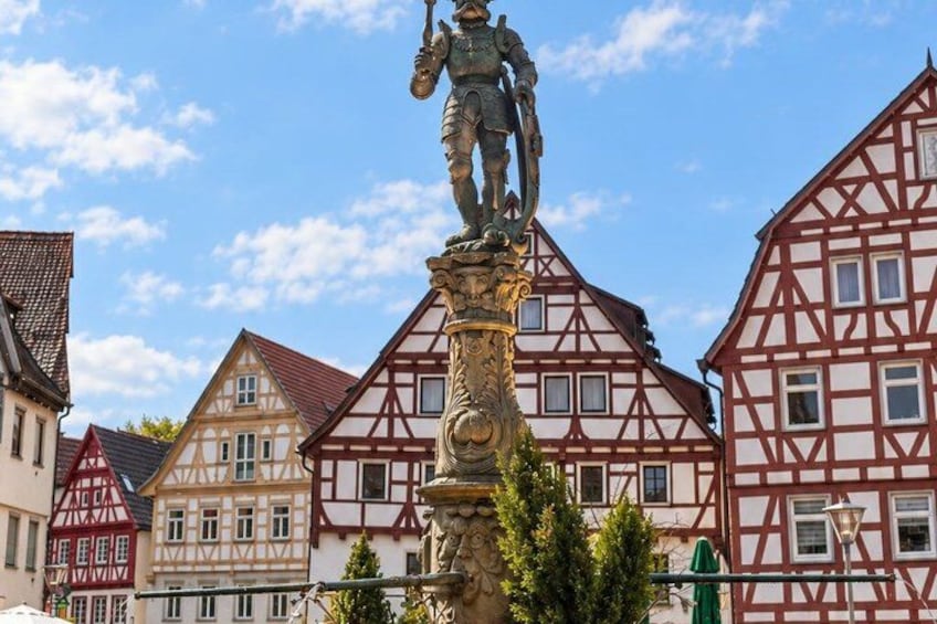 A town square with a statue, traditional half-timbered houses, and a clear sky. 5